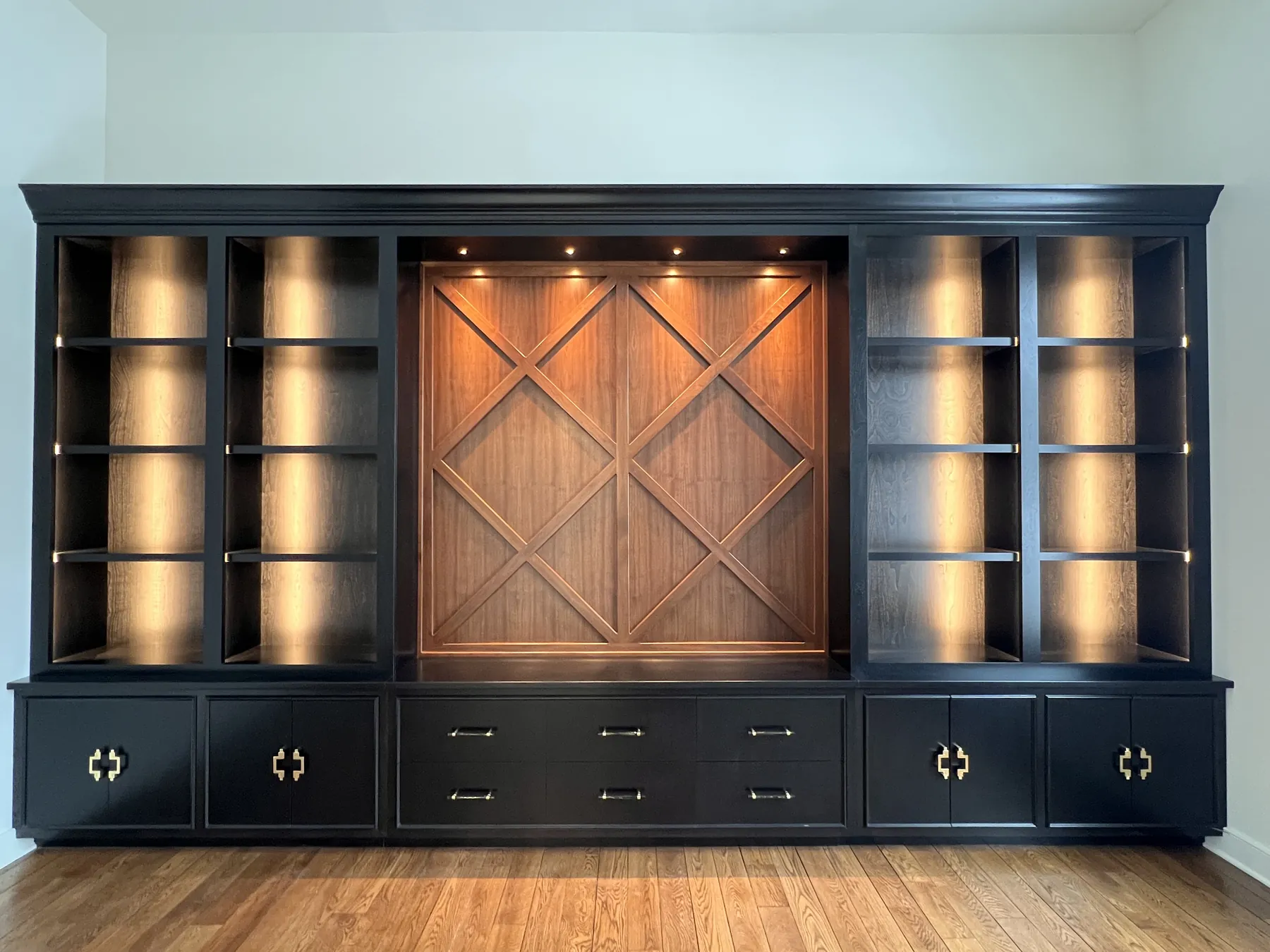 Black built-in wall with lit shelves flanking a stained lattice panel