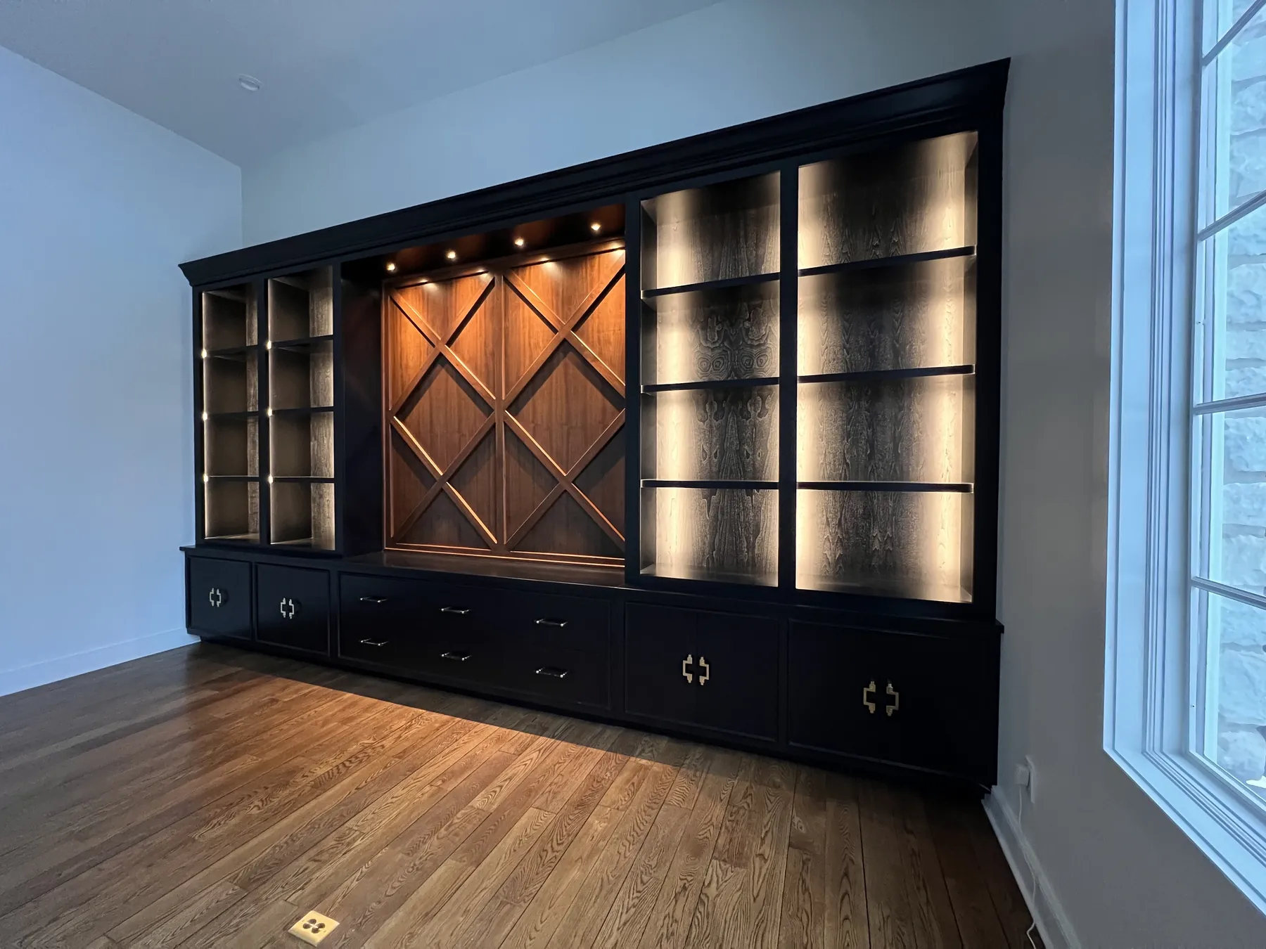 Long black bookcase wall with lit shelves and a stained lattice centre