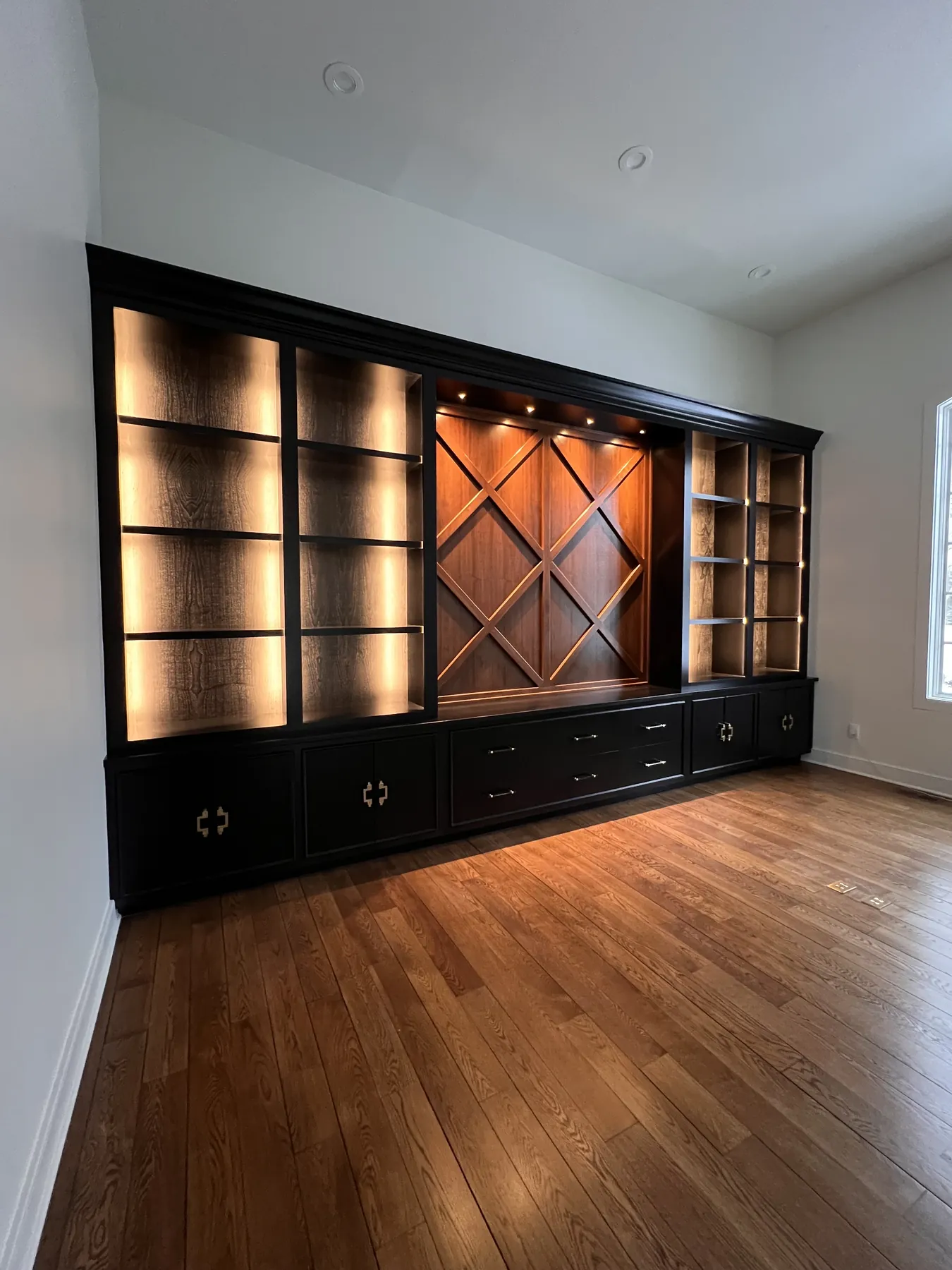 Black built-ins with warm lit shelving either side of the lattice panel