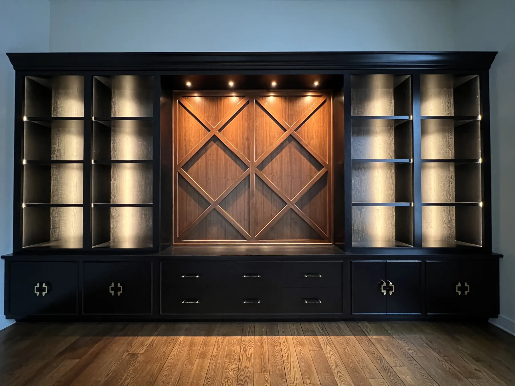 Black media wall with a stained lattice panel and lit display shelves