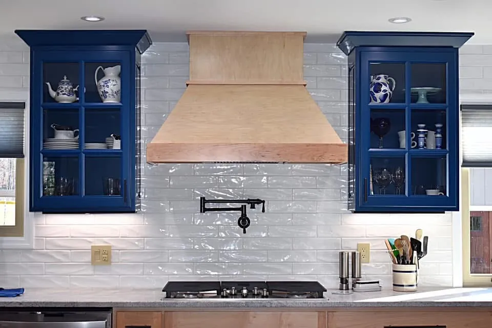 Blue glass-front cabinets flanking a natural maple hood over a pot filler