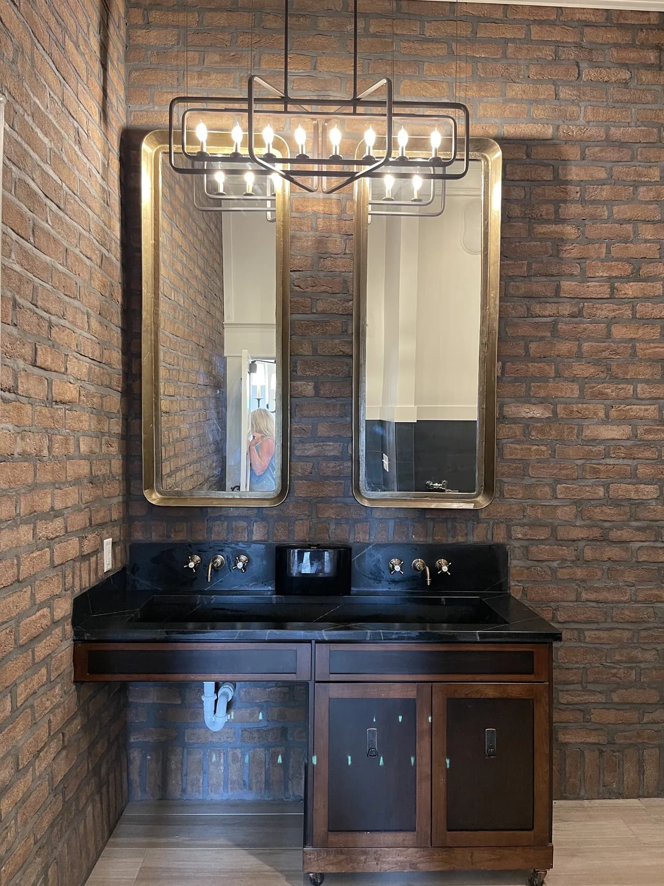 Stained double vanity with a black stone top against an exposed brick wall