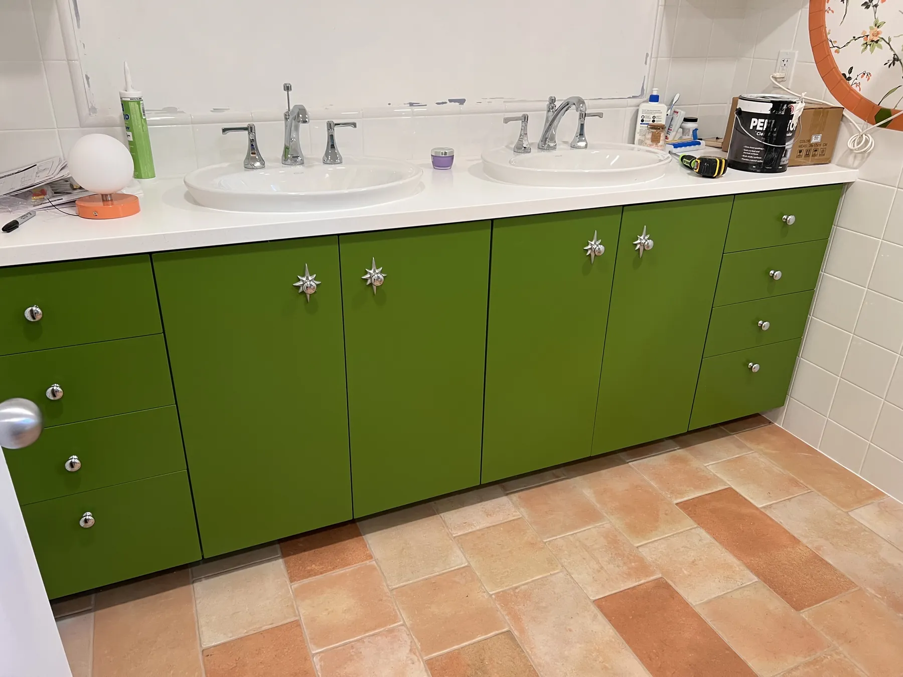 Green lacquered double vanity with starfish knobs over terracotta tile