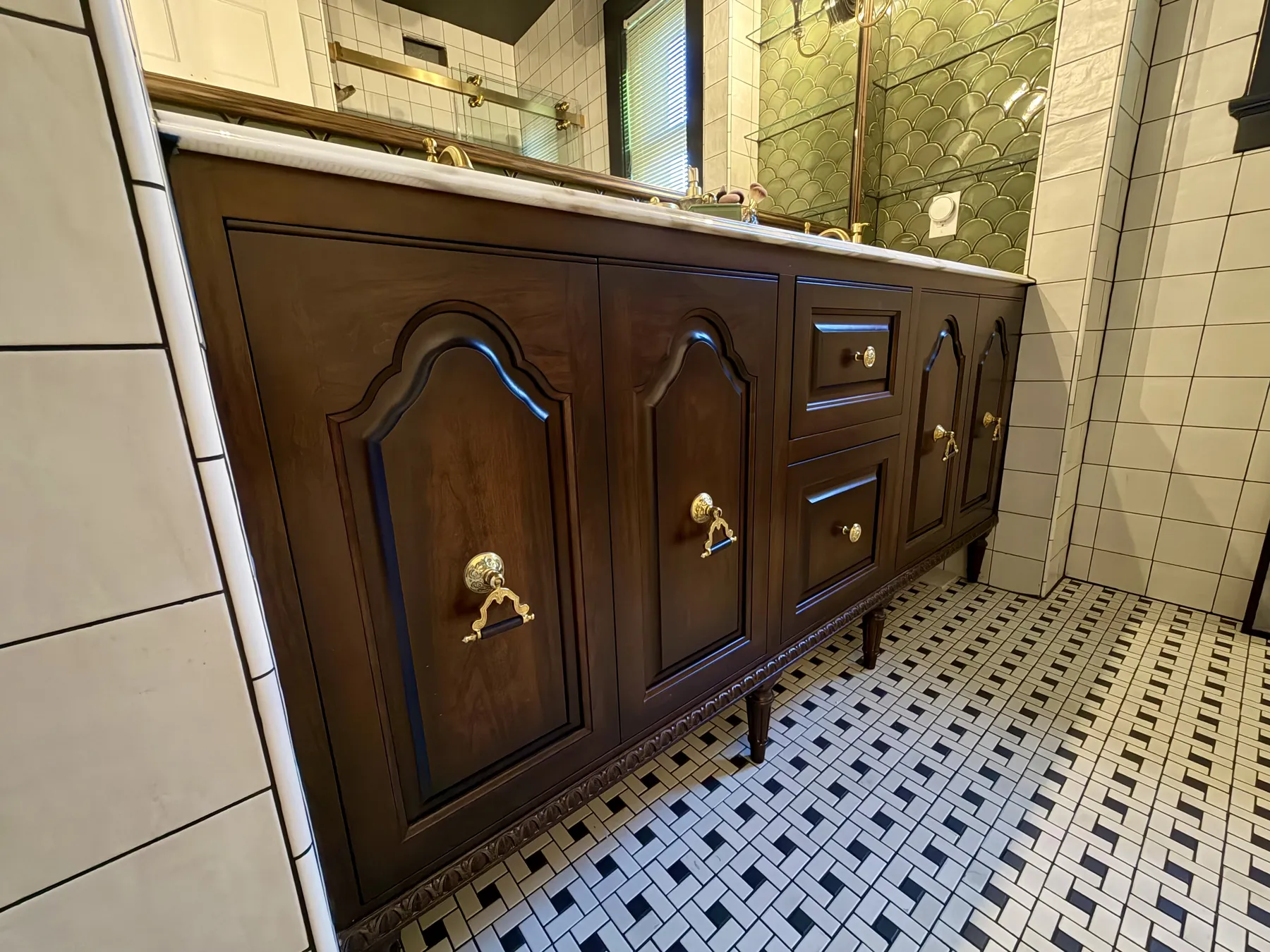 Raised-panel stained vanity with brass hardware on basketweave tile