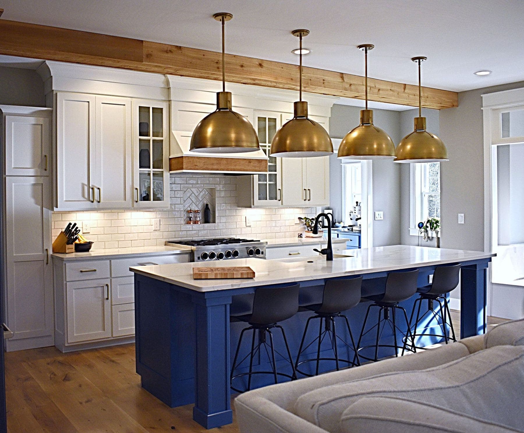 White shaker kitchen with a navy blue island, quartz countertops and four brass dome pendant lights