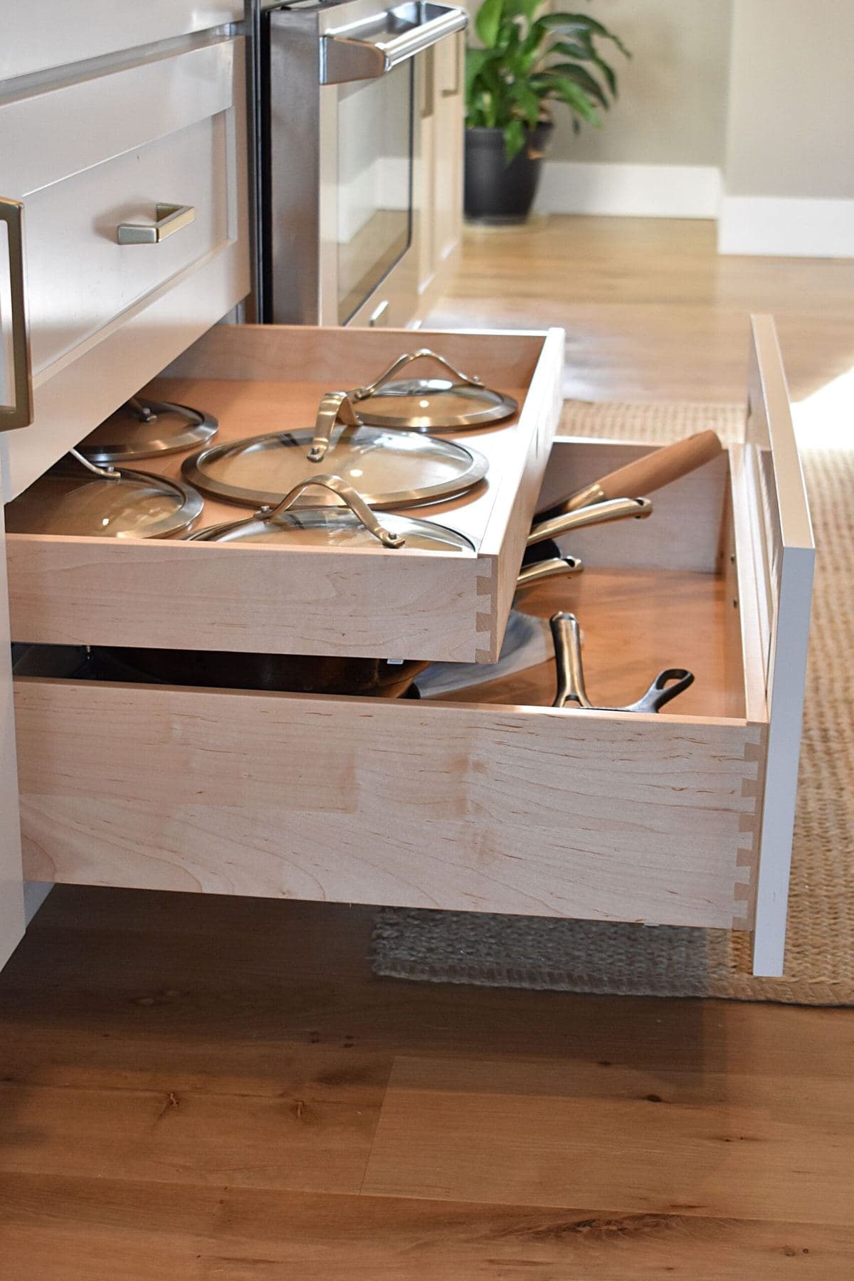 Open two-tier kitchen drawer with dovetailed maple sides holding pans and a separate tray of lids