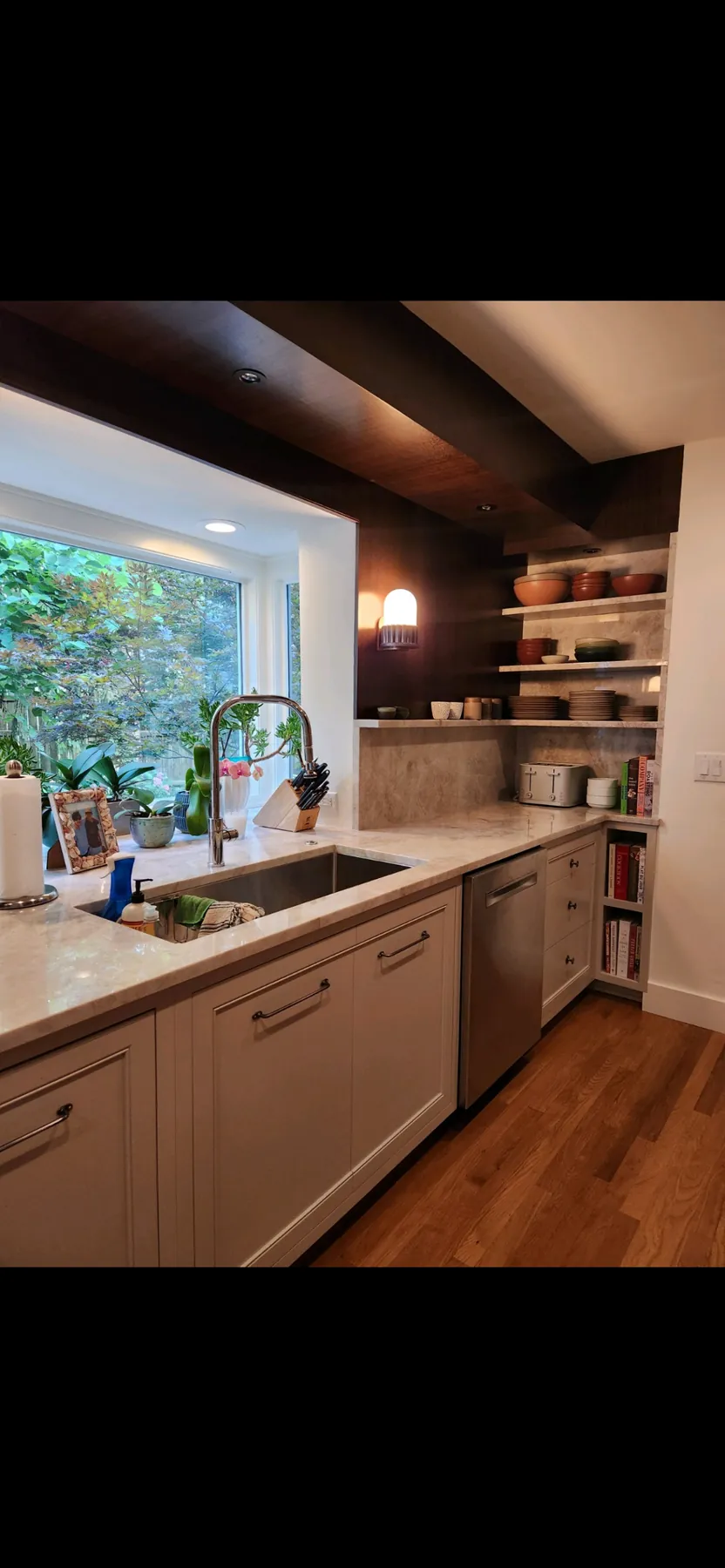 Painted sink run with marble counters and open shelves under the window