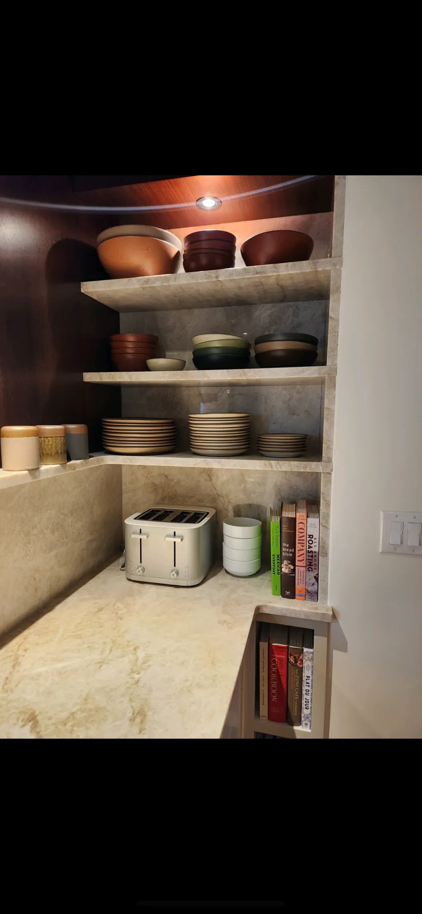 Open marble shelving stacked with dishes above the counter