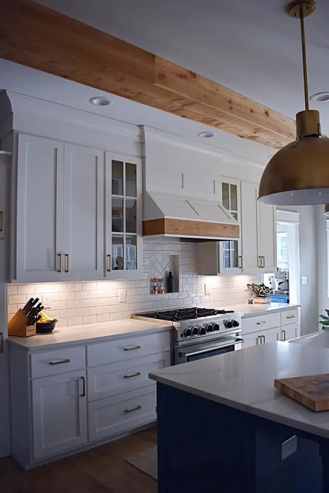 White shaker cabinets and a wood-wrapped hood beside the navy island