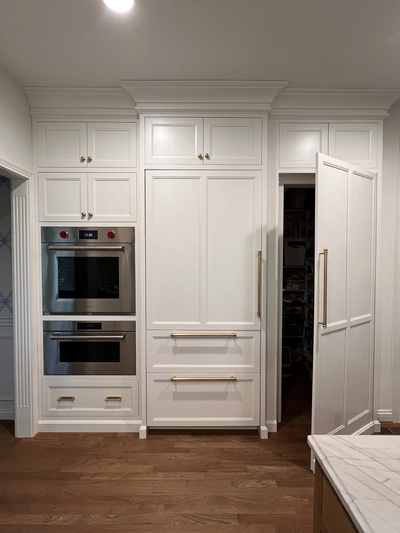 Painted tall cabinetry housing double ovens beside a panelled fridge