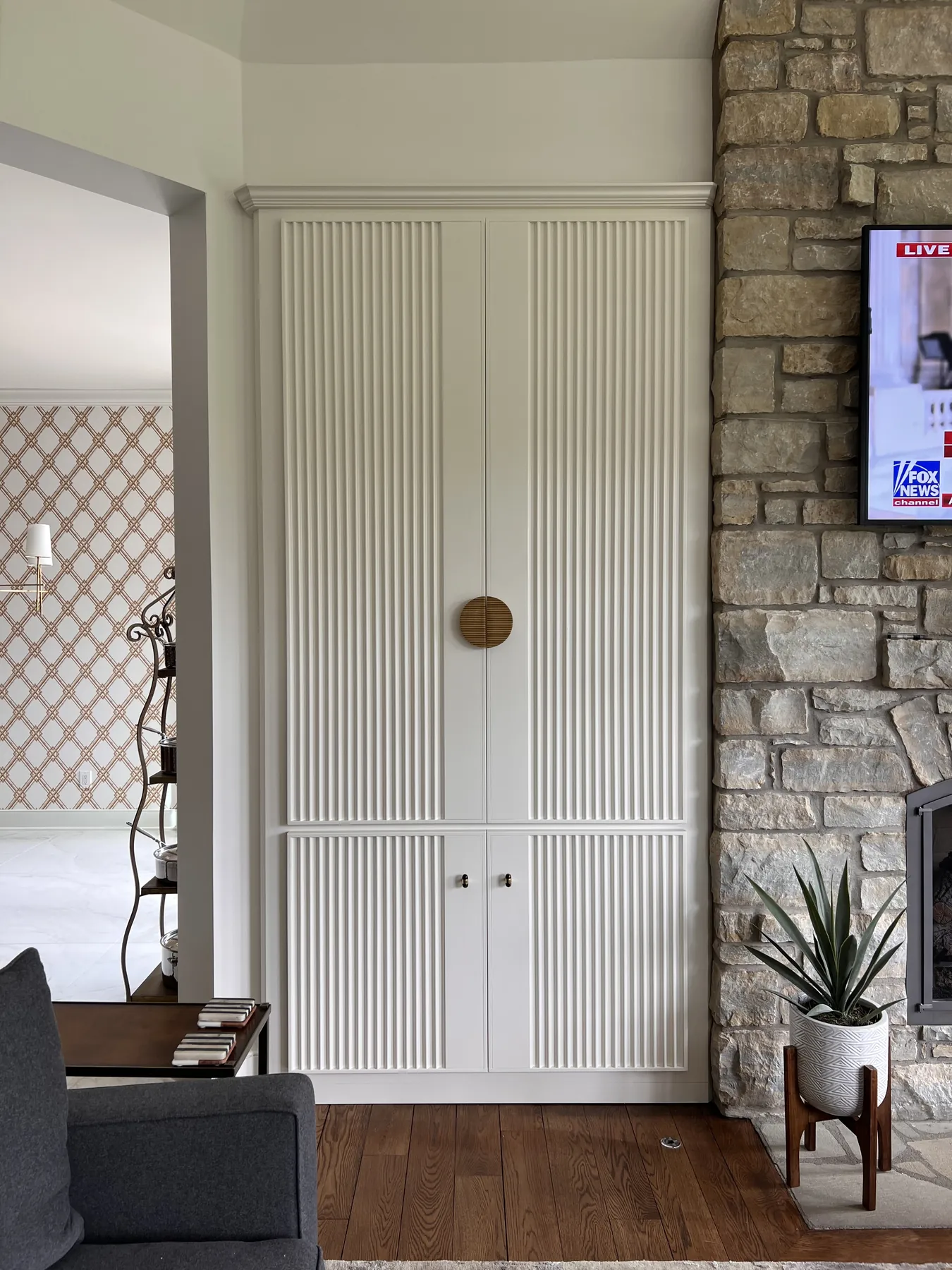 Tall reeded painted cabinet with a brass knob beside the stone hearth