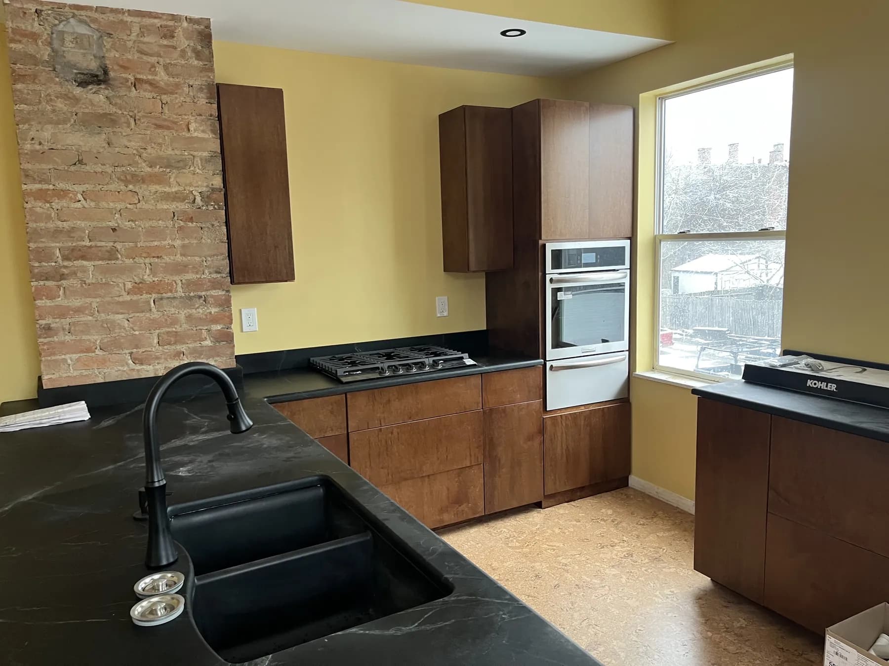 Stained kitchen with black stone counters against an exposed brick chimney
