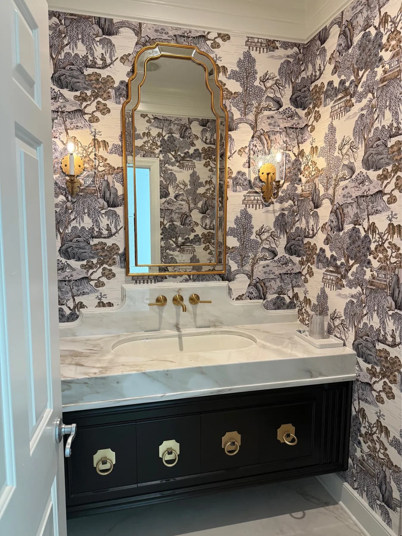 Toile papered powder room with a black vanity and gilt mirror