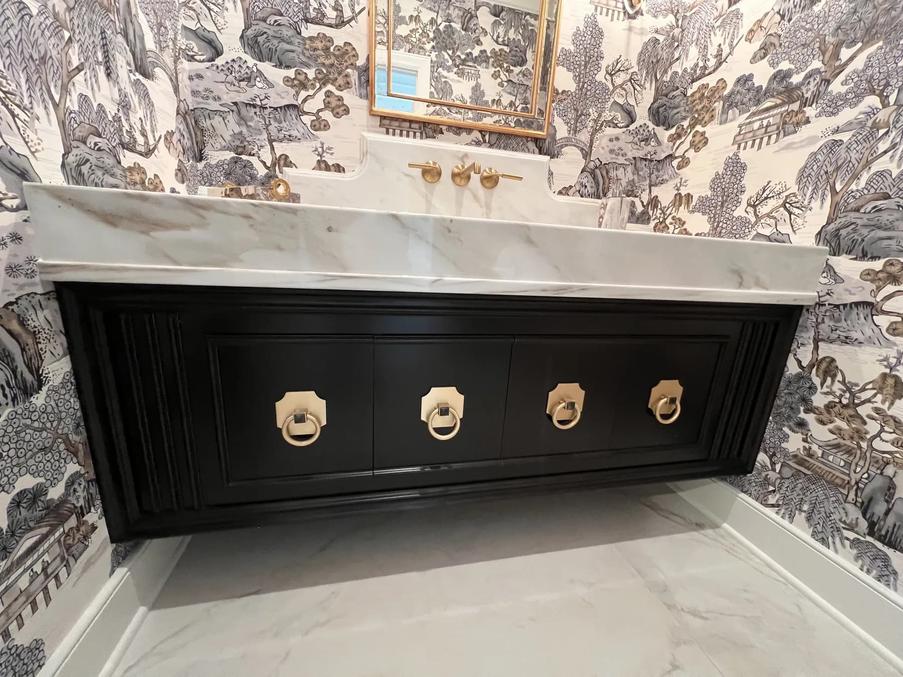 Black vanity with brass ring pulls beneath a marble top and toile paper