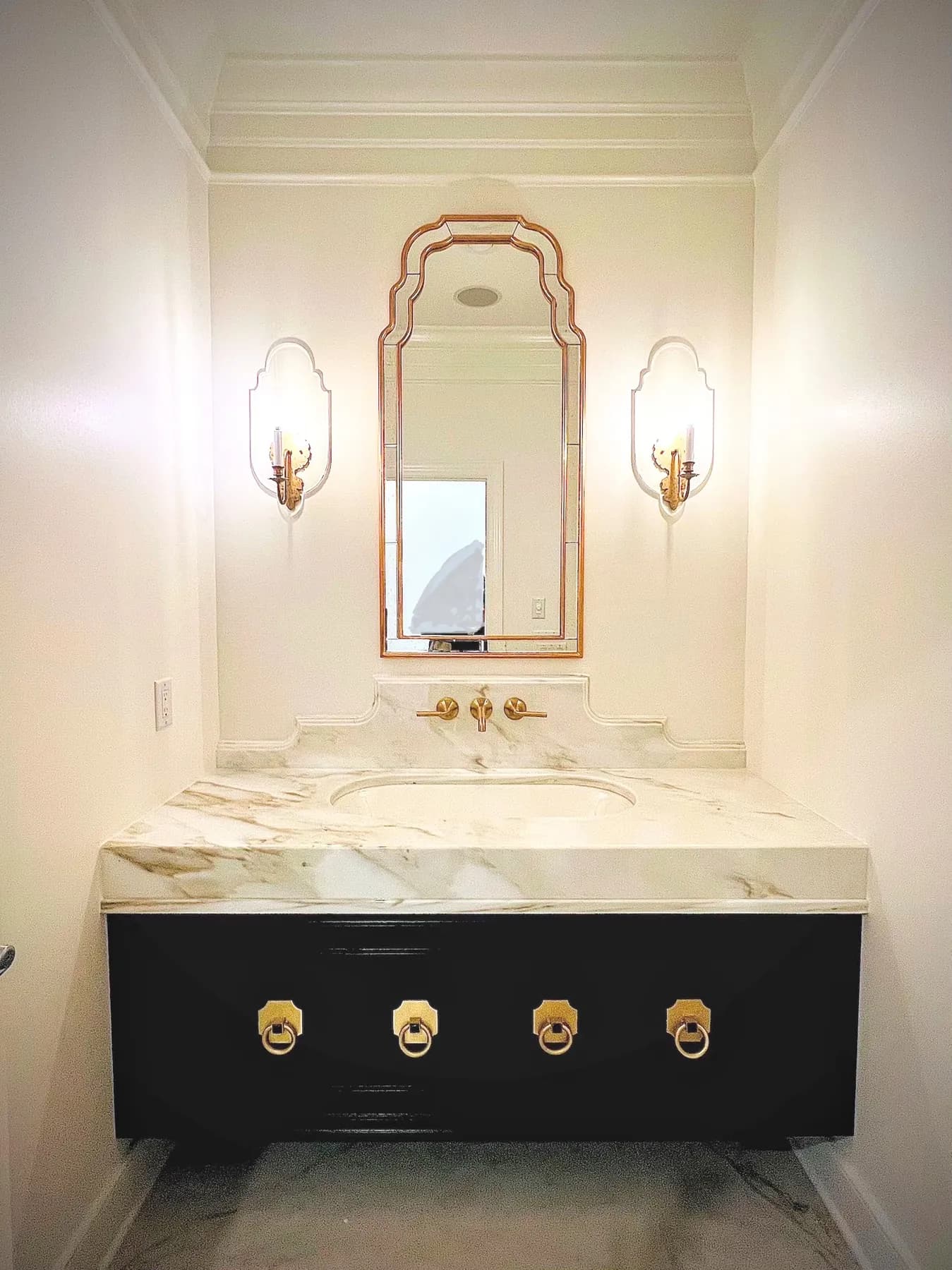 Black vanity with brass ring pulls under an arched mirror