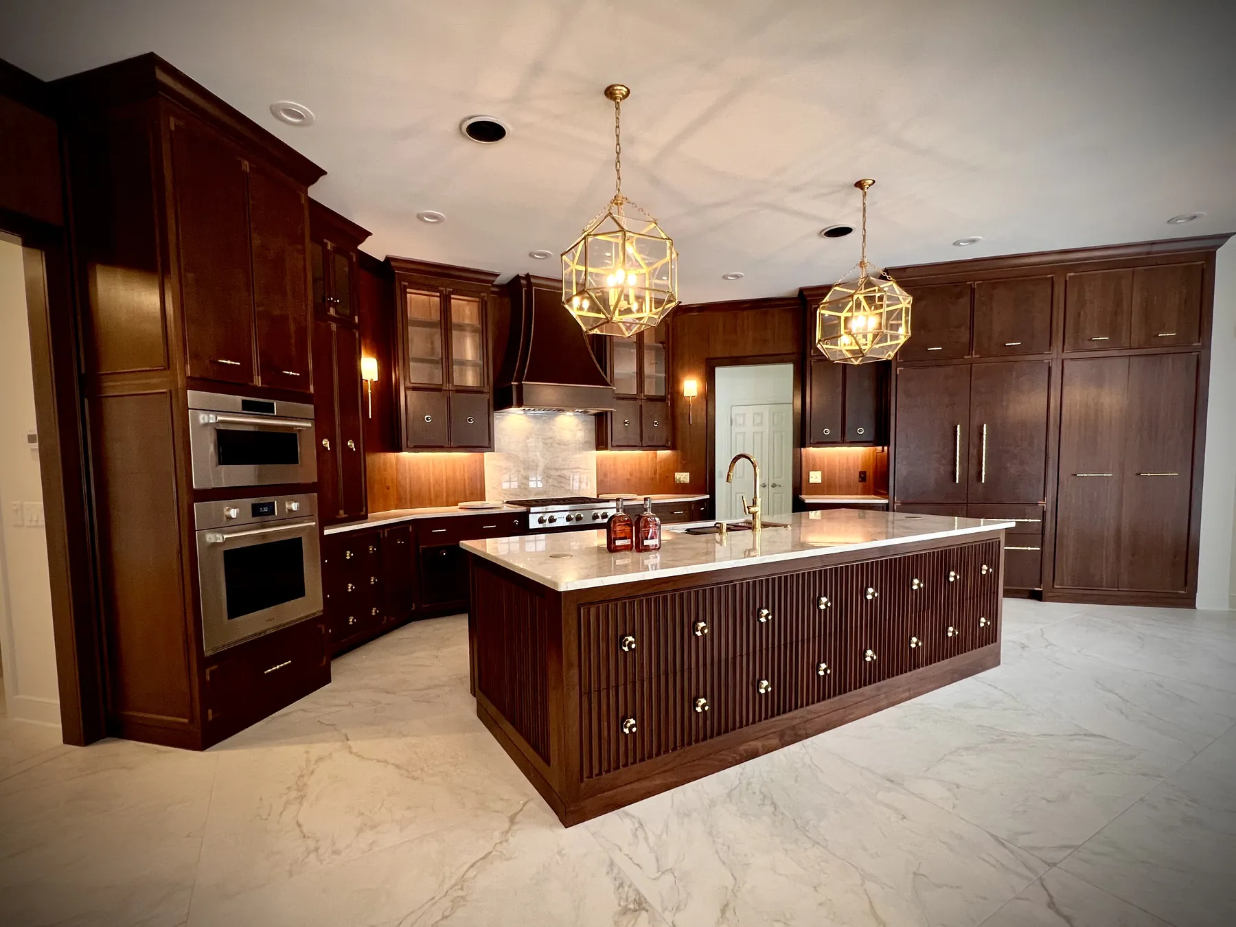 Stained walnut kitchen with a long reeded island, marble counters and two gold lantern pendants