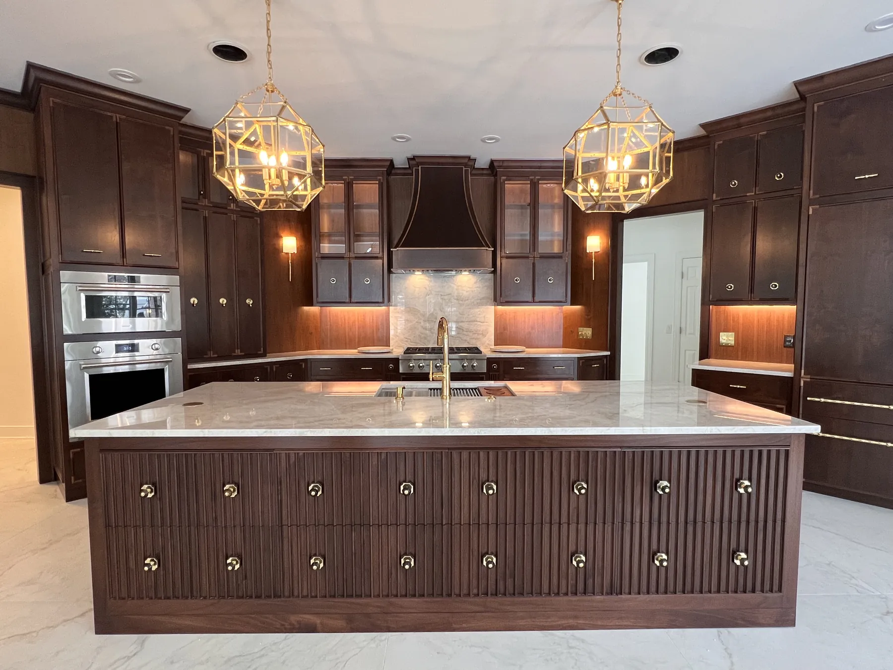 Wide view of the walnut kitchen island with reeded drawer fronts under gold lanterns