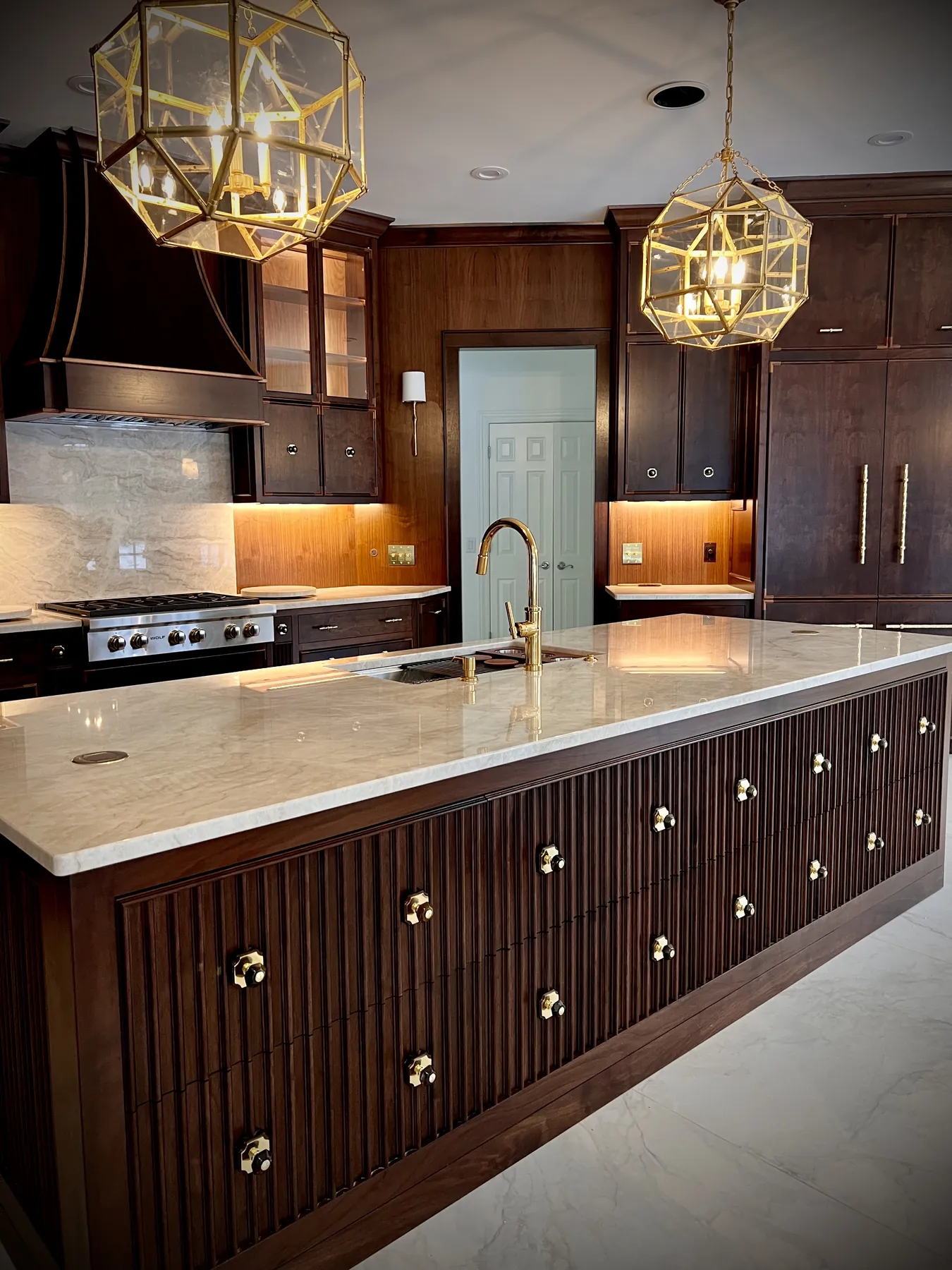 Walnut kitchen range wall with a panelled hood, marble splash and brass faucet