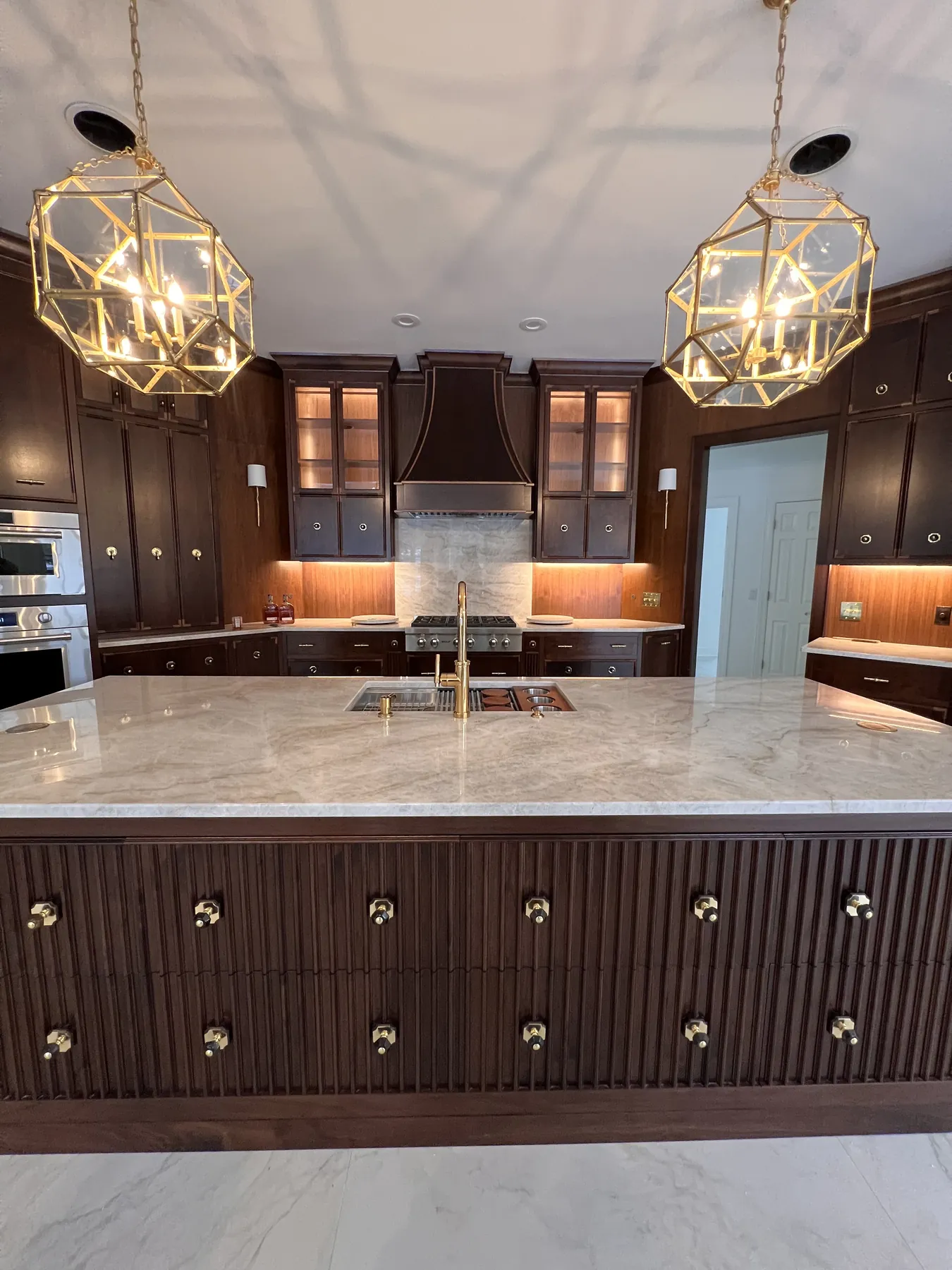 Marble island top and reeded walnut drawer bank beneath gold lantern pendants