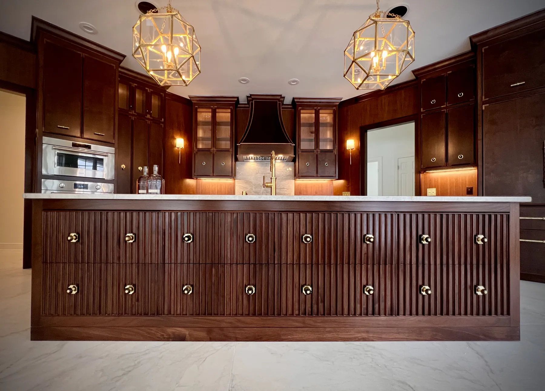 Walnut kitchen run with glass-front cabinets, integrated ovens and a reeded island