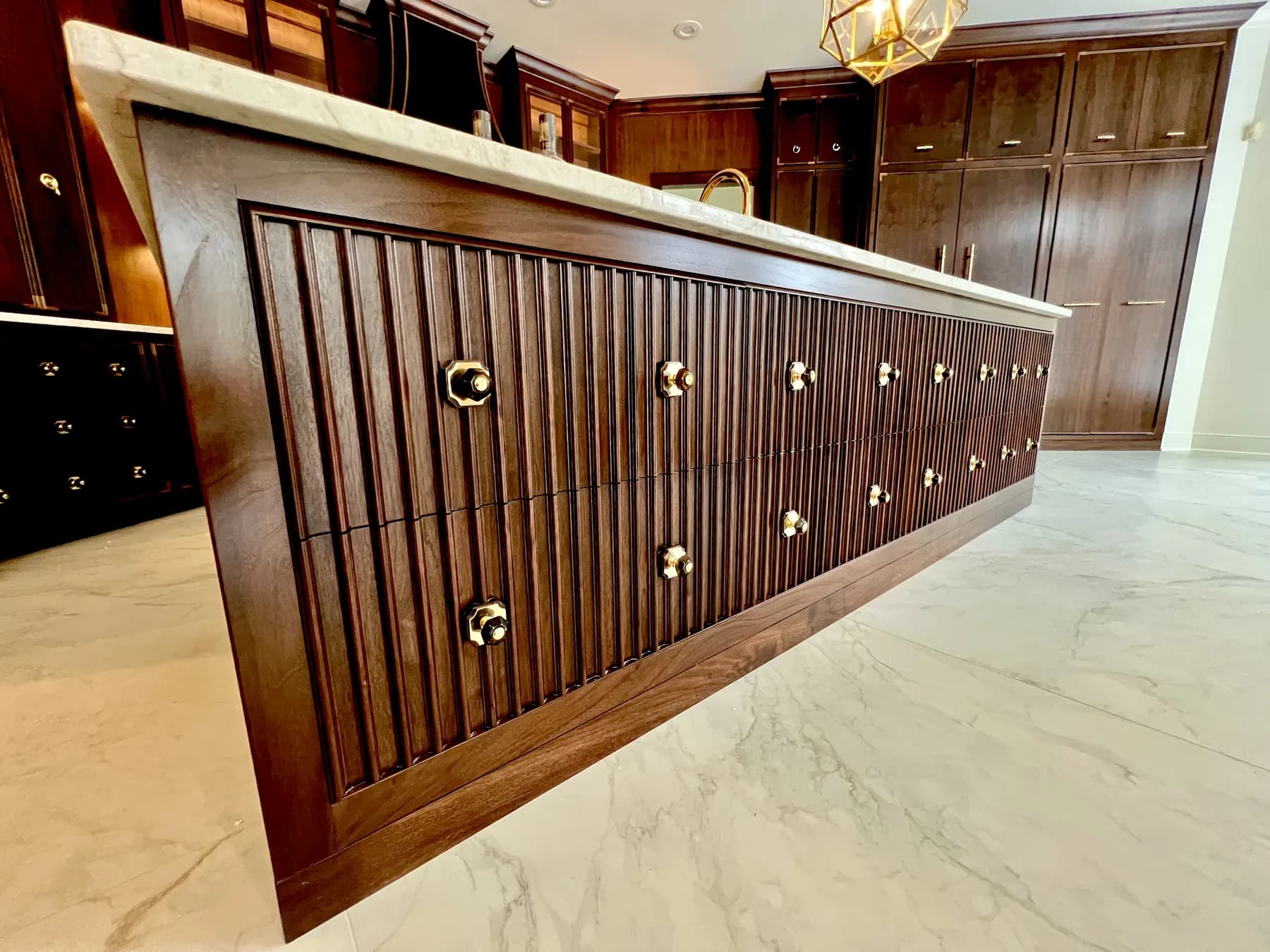 Reeded walnut island with brass knobs running the length of the marble top