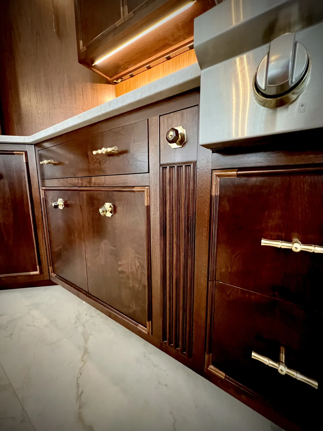 Corner of the reeded walnut island with brass knobs and a marble edge