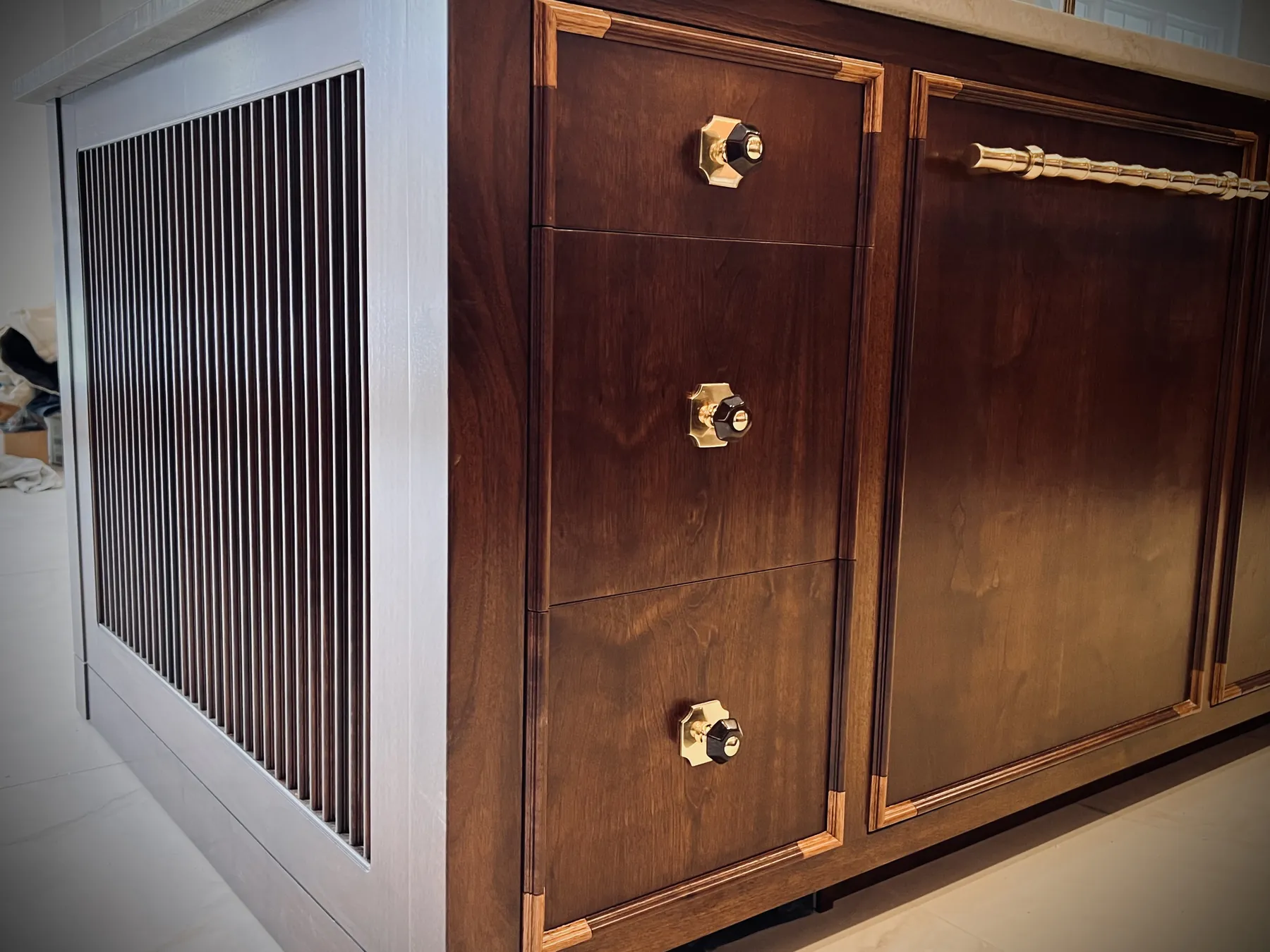 Detail of reeded panelling beside brass-knobbed walnut drawers with inlaid banding