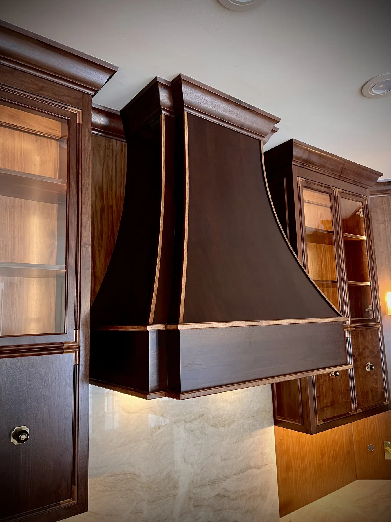 Curved walnut range hood flanked by glass-front cabinets