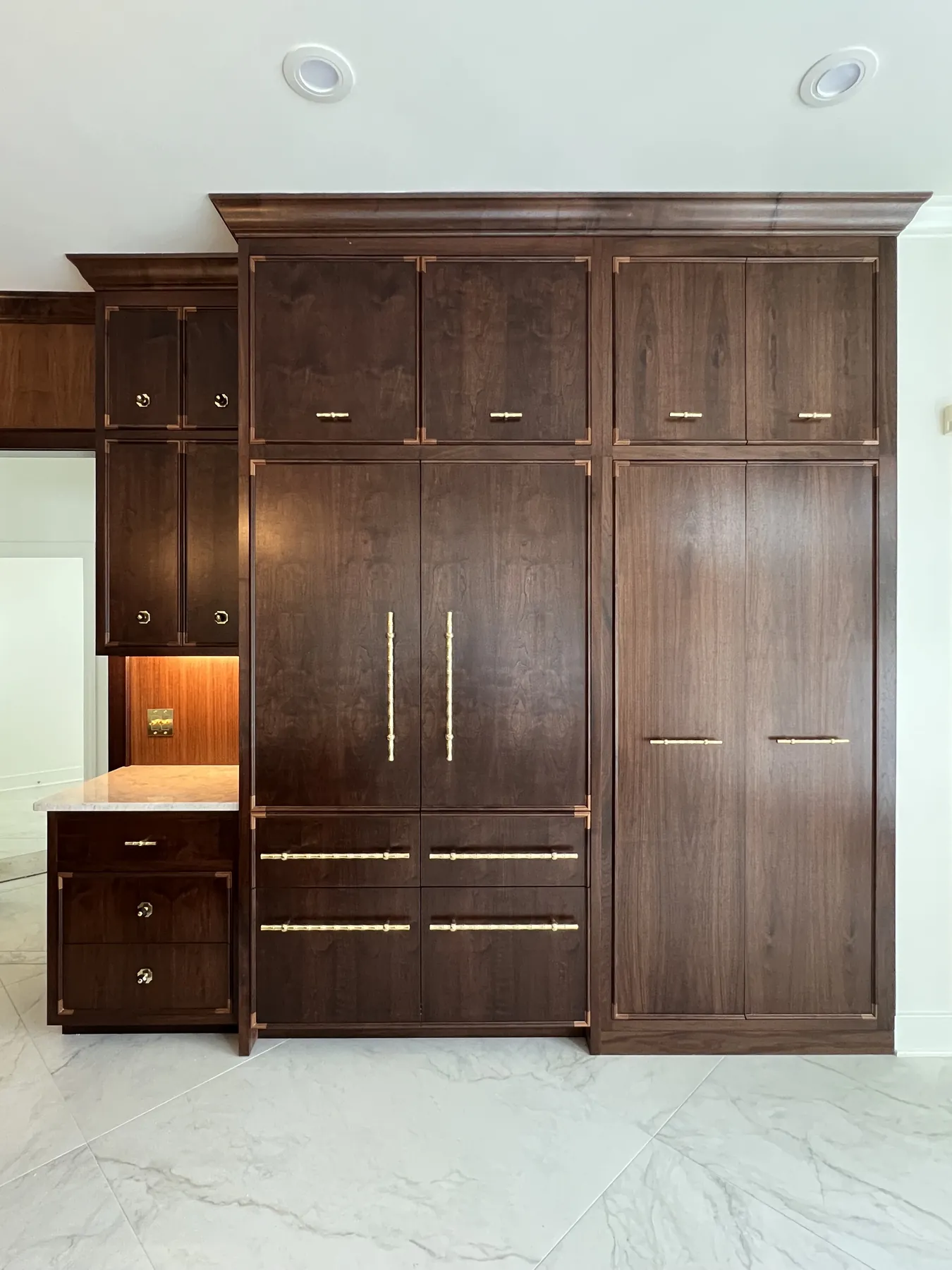 Full wall of walnut pantry cabinetry with brass bar pulls