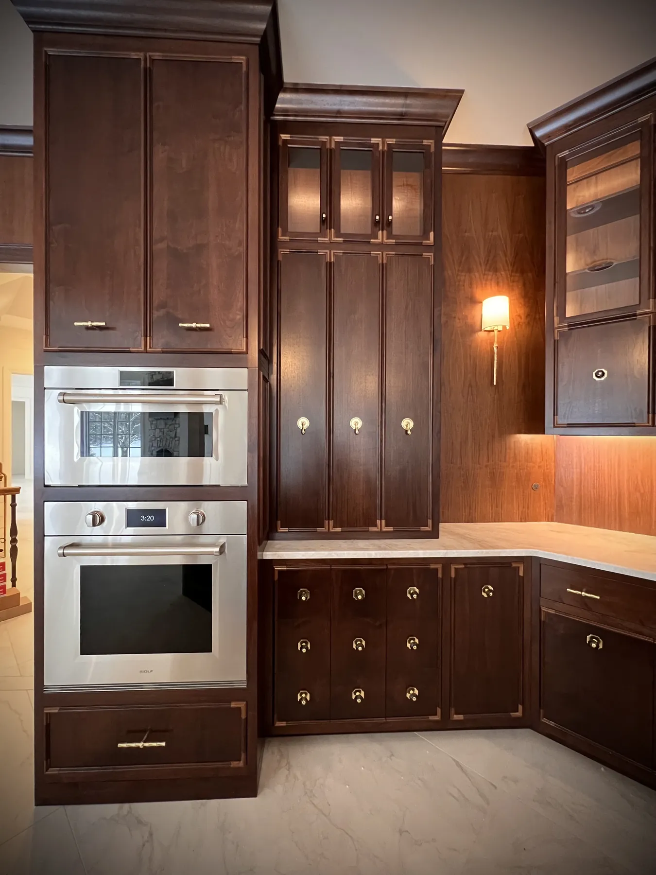 Walnut cabinetry framing double wall ovens and a lit counter niche