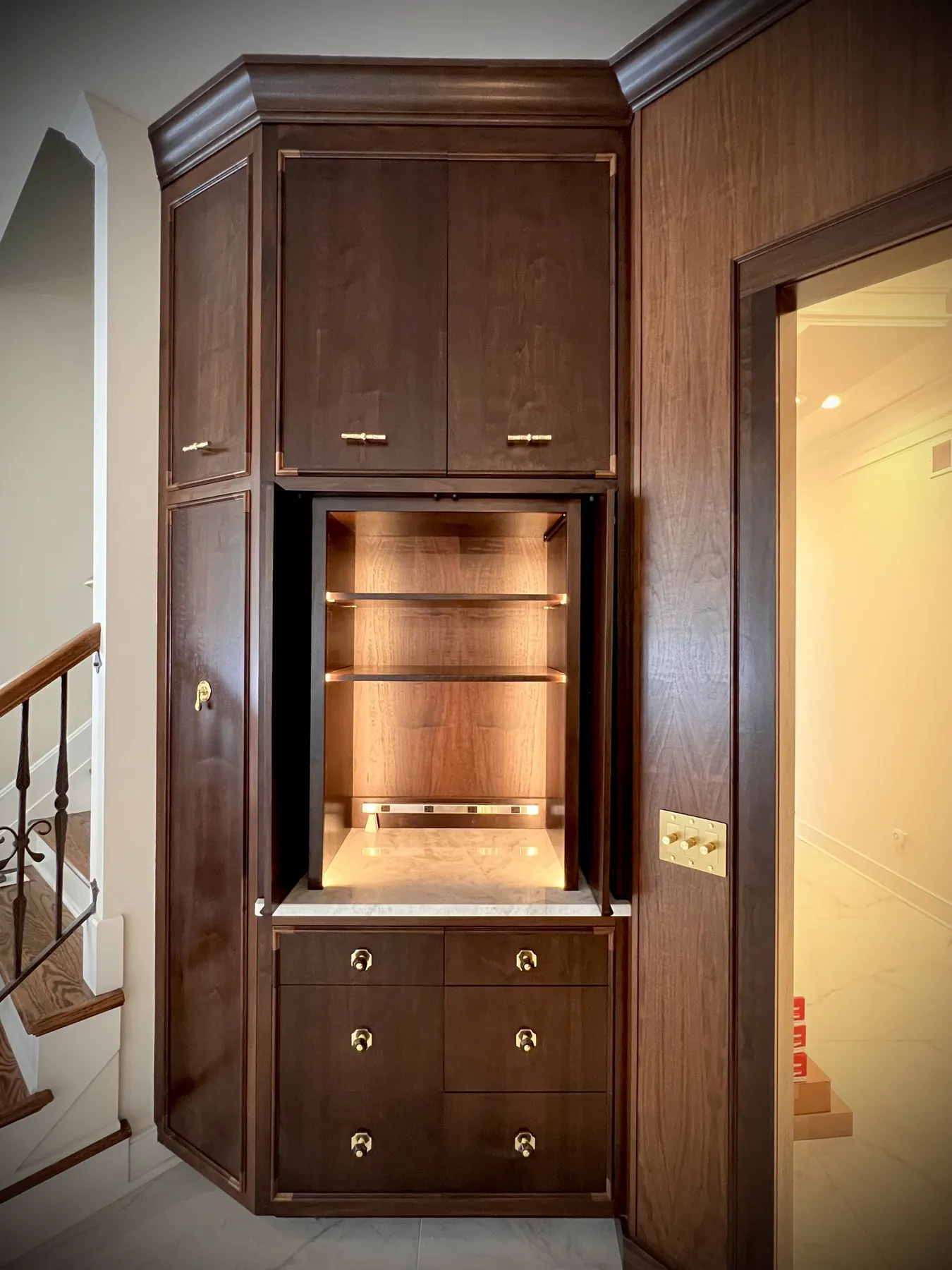 Lit walnut niche between tall cabinets beside a stair rail