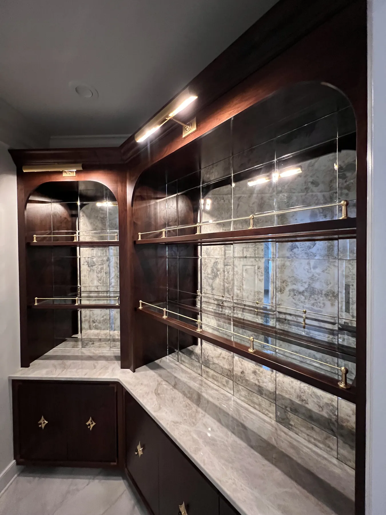 Arched antiqued mirror bar with brass rails and lit shelves