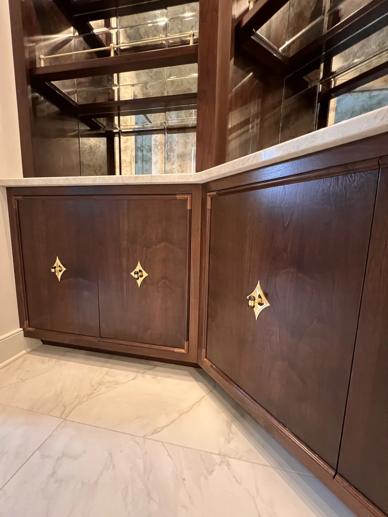 Walnut cabinetry with gilded inlay diamonds beneath antiqued mirror panels