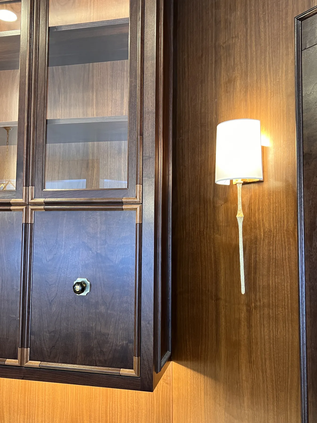 Two brass sconces on walnut panelling beside a glazed cabinet