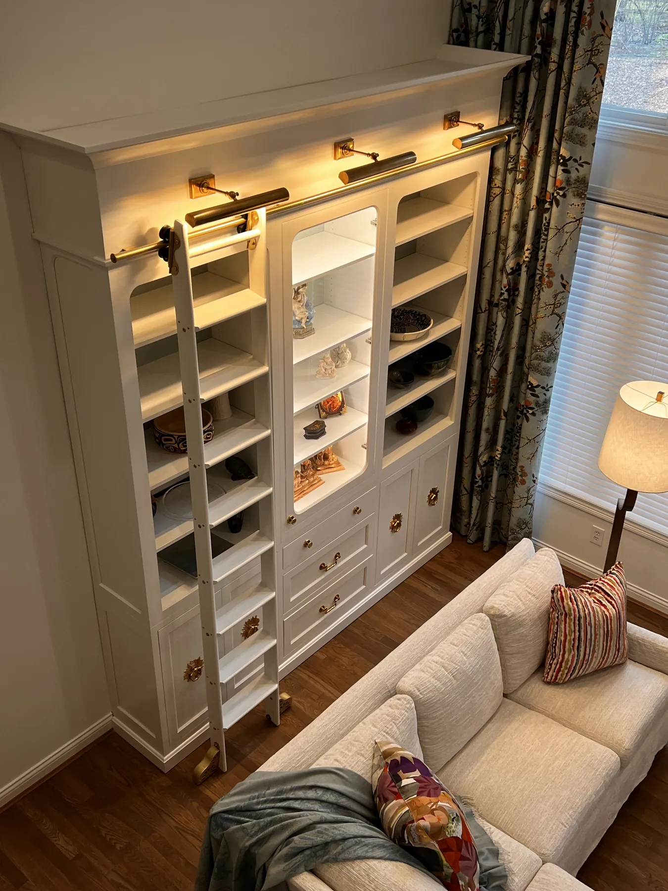 Painted library wall with a brass rolling ladder, lit shelves and cabinets below