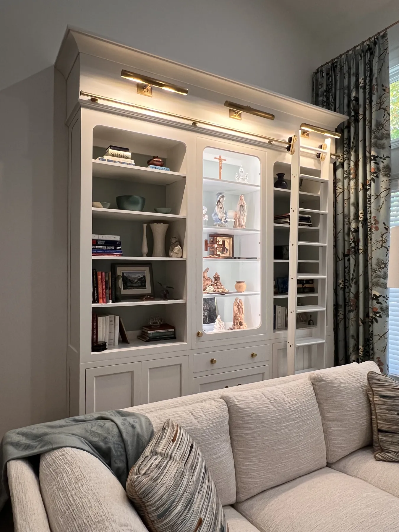 Floor-to-ceiling painted bookcase with a brass ladder rail above the sofa