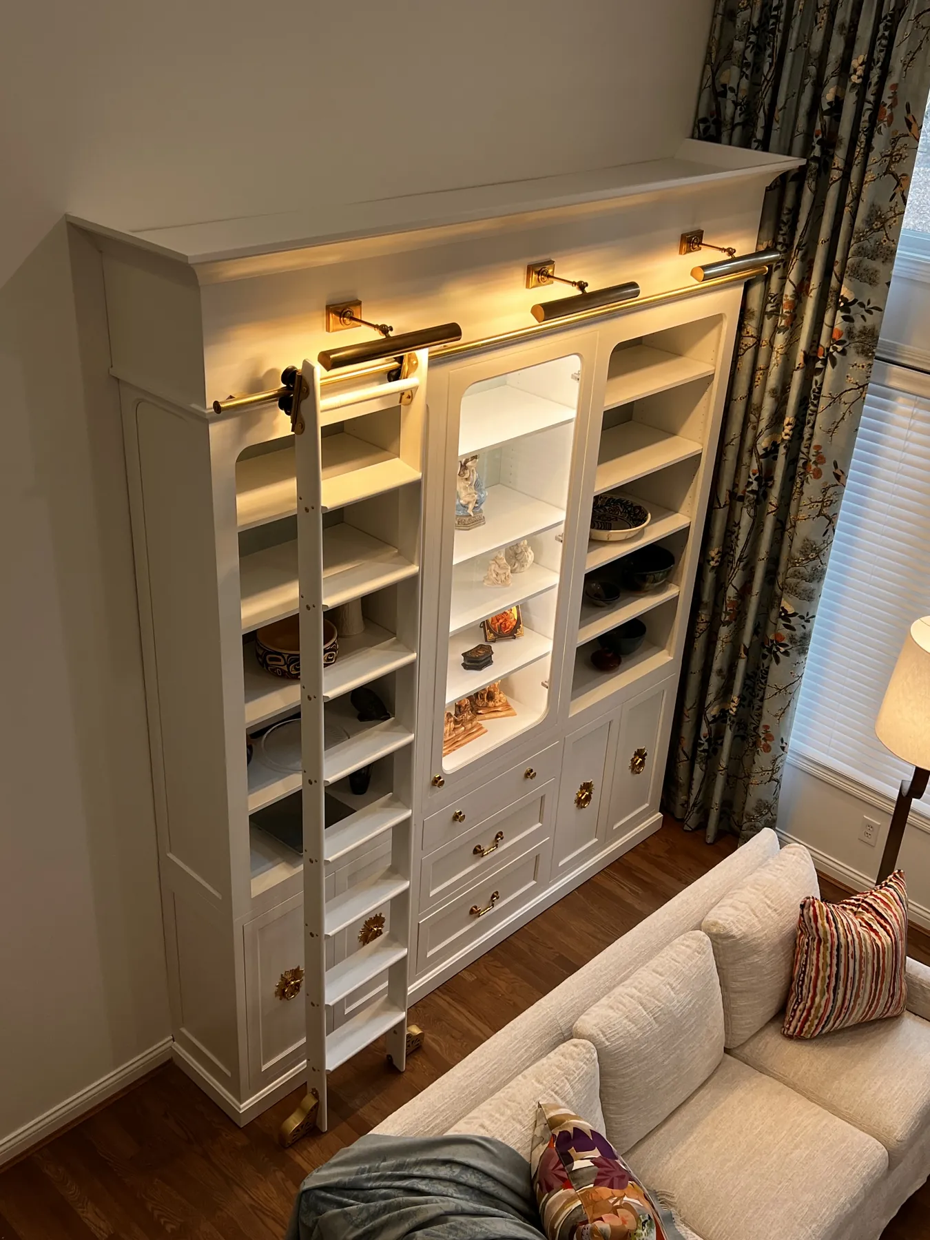 Painted library shelving with a rolling ladder and picture lights