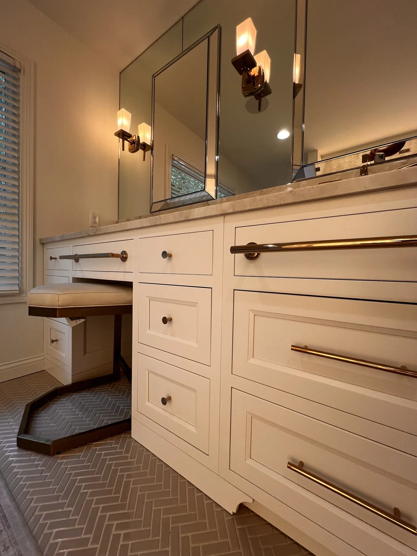 Painted vanity with a marble top, brass pulls and a built-in makeup seat