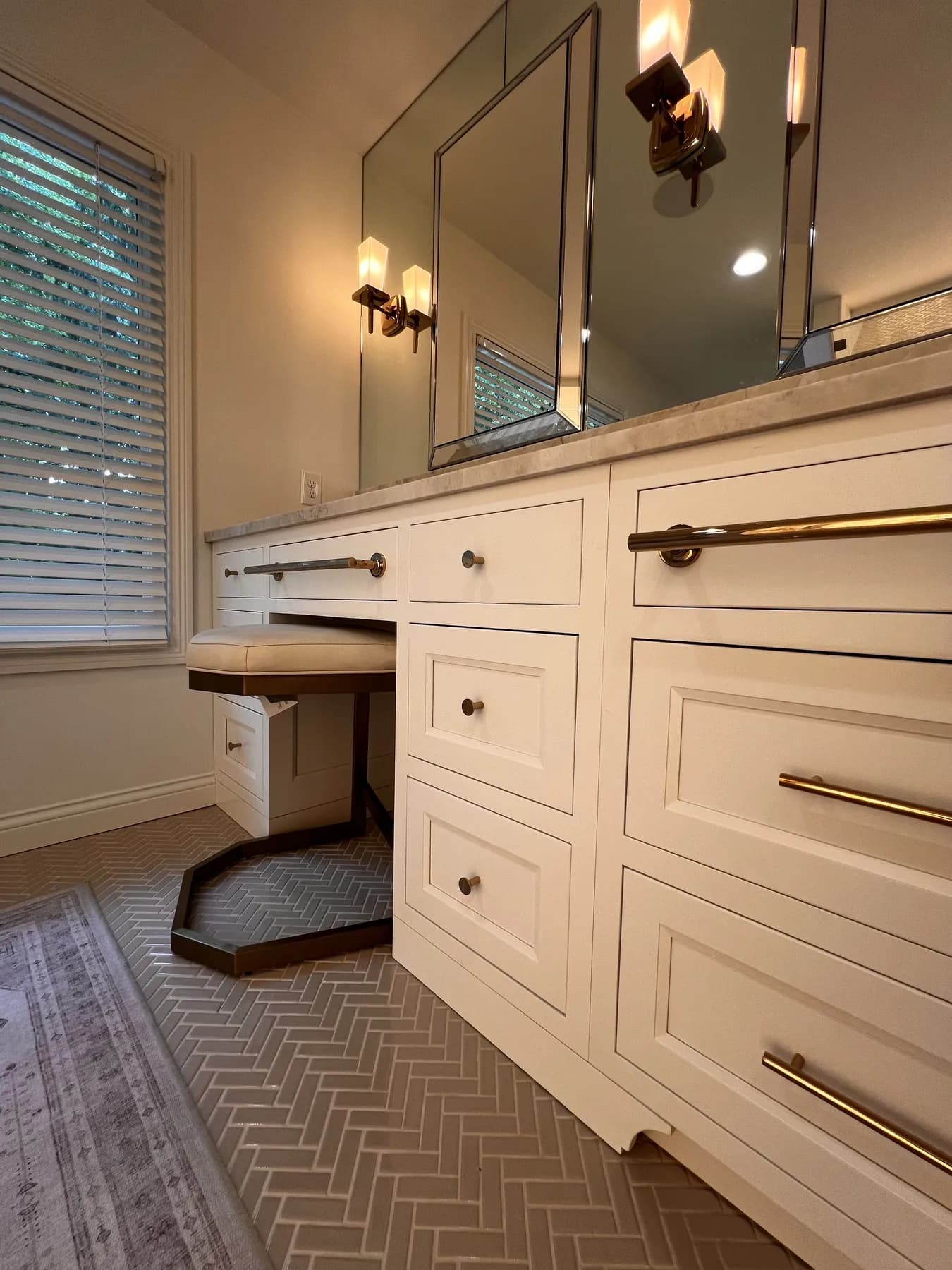 Makeup seat tucked under the painted vanity beside banks of brass-pulled drawers