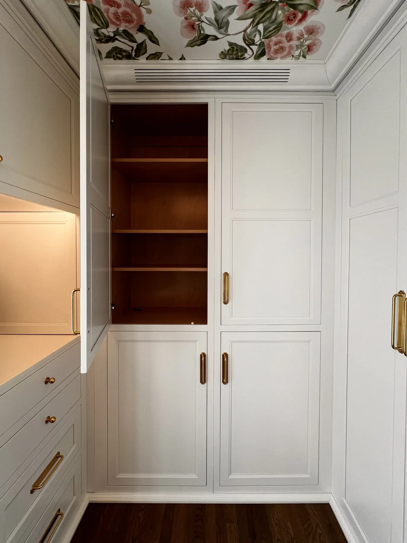 Tall painted cabinets with brass pulls opening to stained interior shelving