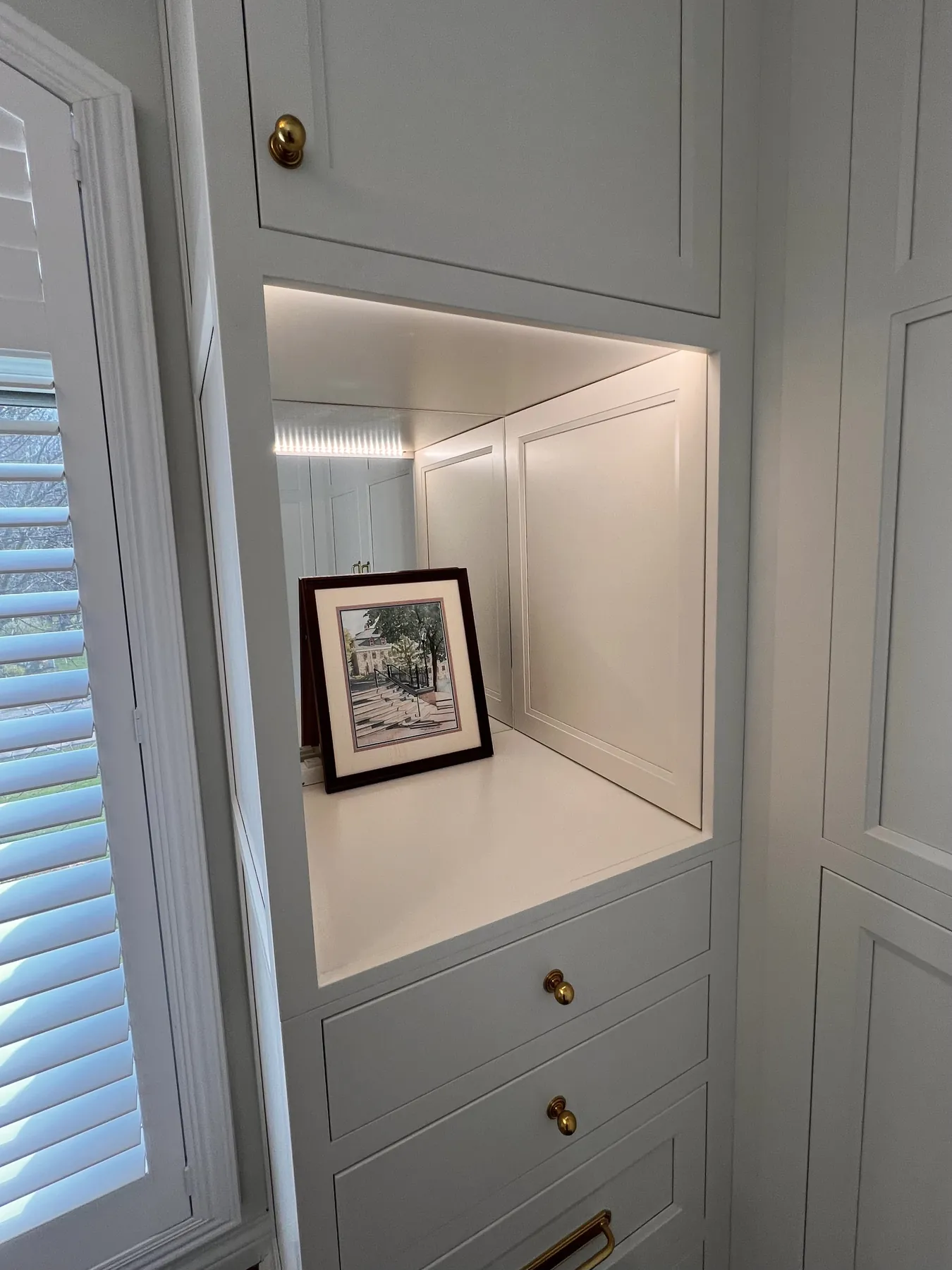 Painted built-in shelving lit beside louvred shutters