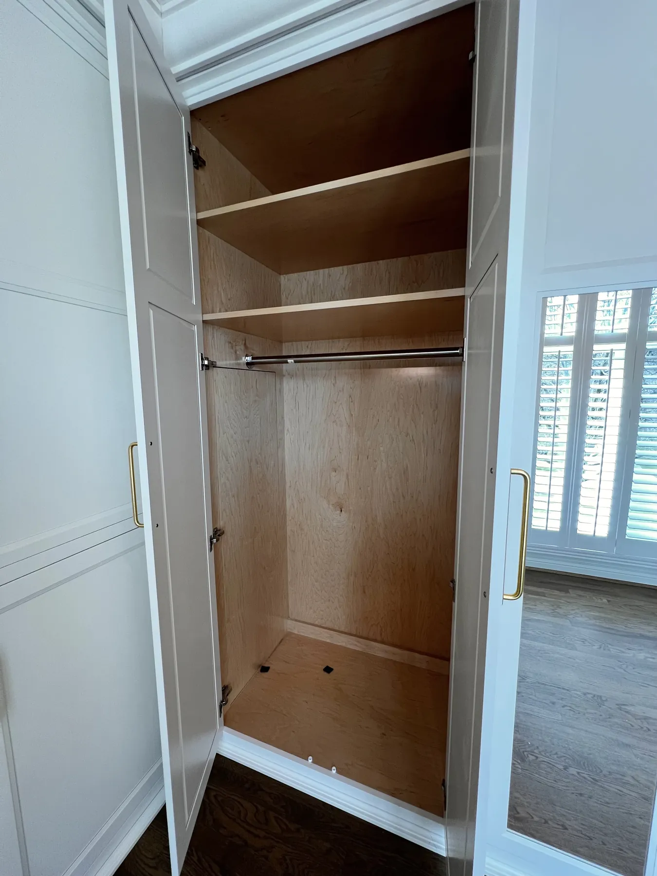 Painted closet doors open to hanging rods and stained shelving